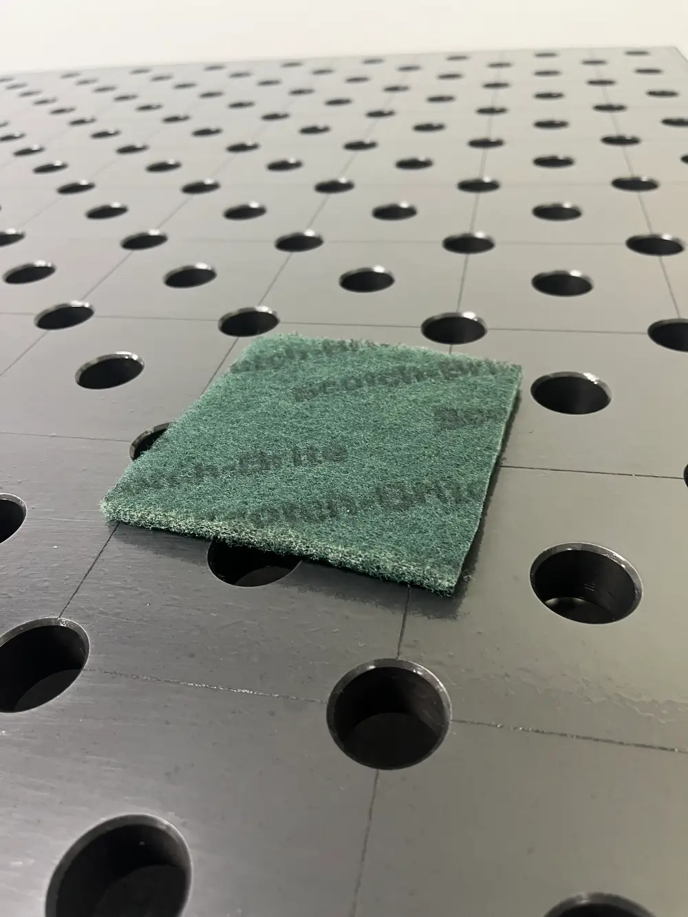 Scotchbrite pad used to clean small buildup from welding table surface